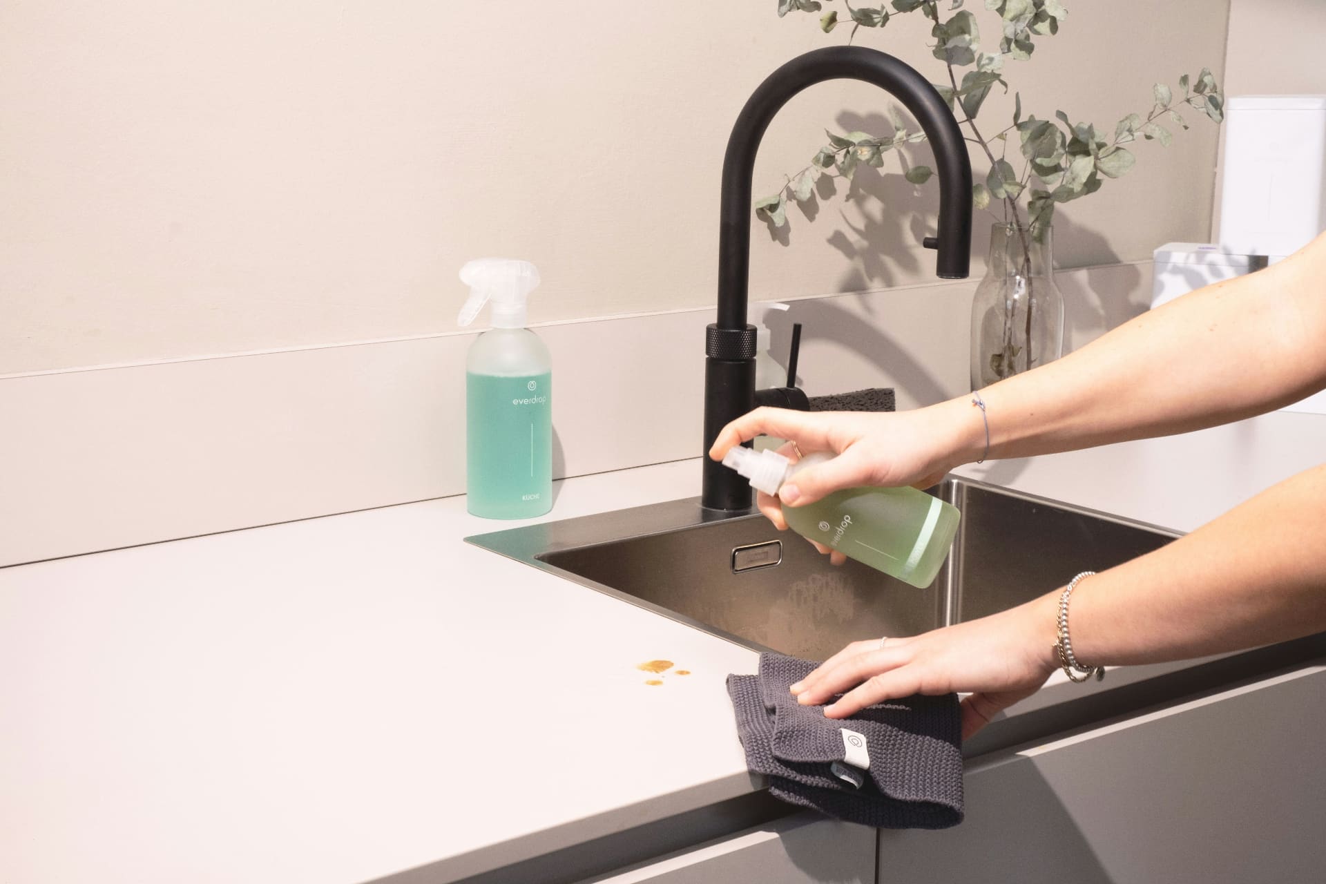 Hands spraying eco-friendly cleaner and wiping a modern kitchen worktop beside a black tap — social media agency for cleaning companies