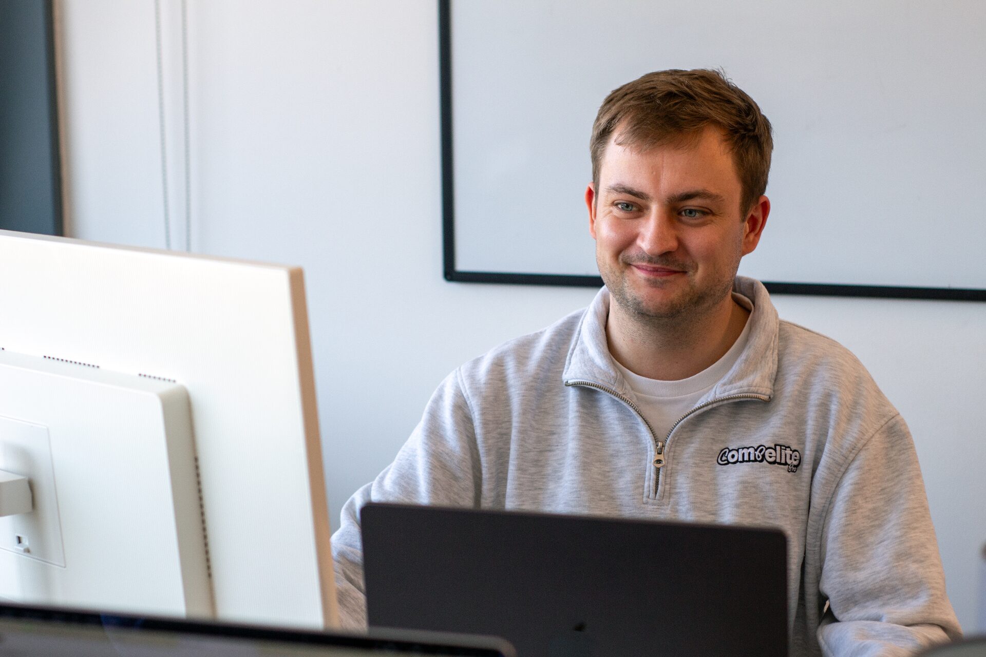 Compelite Pro team member smiling at laptop in branded sweater